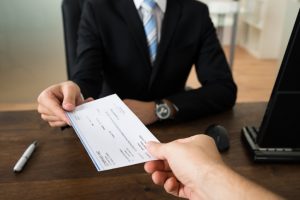 Close-up Of Businessman Hands Giving Cheque To Other Person In Office